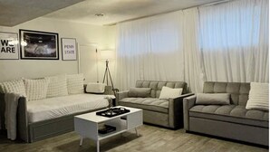 A modern living room with a grey sofa, a white coffee table, and a grey couch. There are two framed pictures on the wall and a lamp on a side table.