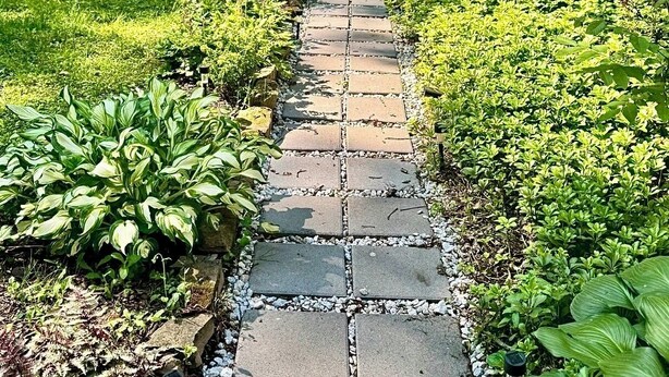 A stone pathway leading to a garden area with a table and chairs.