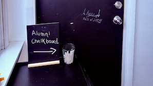 A blackboard with names and dates, a sign reading "Alumni Chalkboard," and a trash can.