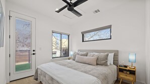 A bedroom with a bed, two bedside tables, a ceiling fan, and two windows. - Downtown - Pool + Family + Deck + FirePit + Pets (Austin)