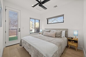 A bedroom with a bed, two bedside tables, a ceiling fan, and two windows. - Downtown - Pool + Family + Deck + FirePit + Pets (Austin)