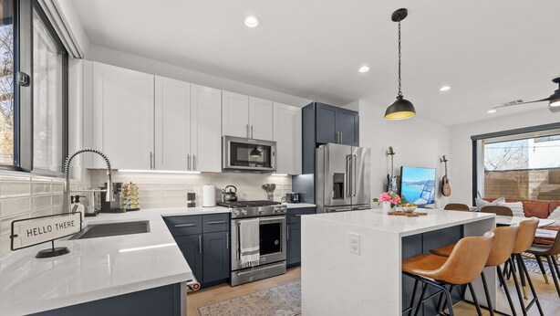 A modern kitchen with white cabinetry, stainless steel appliances, and a central island with bar stools. - Downtown - Pool + Family + Deck + FirePit + Pets (Austin)