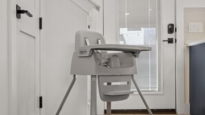 A room with a white door, a window with blinds, and a grey baby high chair. - Downtown - Pool + Family + Deck + FirePit + Pets (Austin)