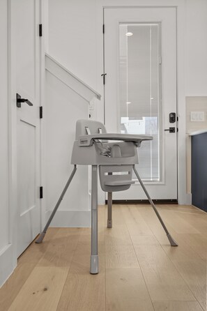 A room with a white door, a window with blinds, and a grey baby high chair. - Downtown - Pool + Family + Deck + FirePit + Pets (Austin)