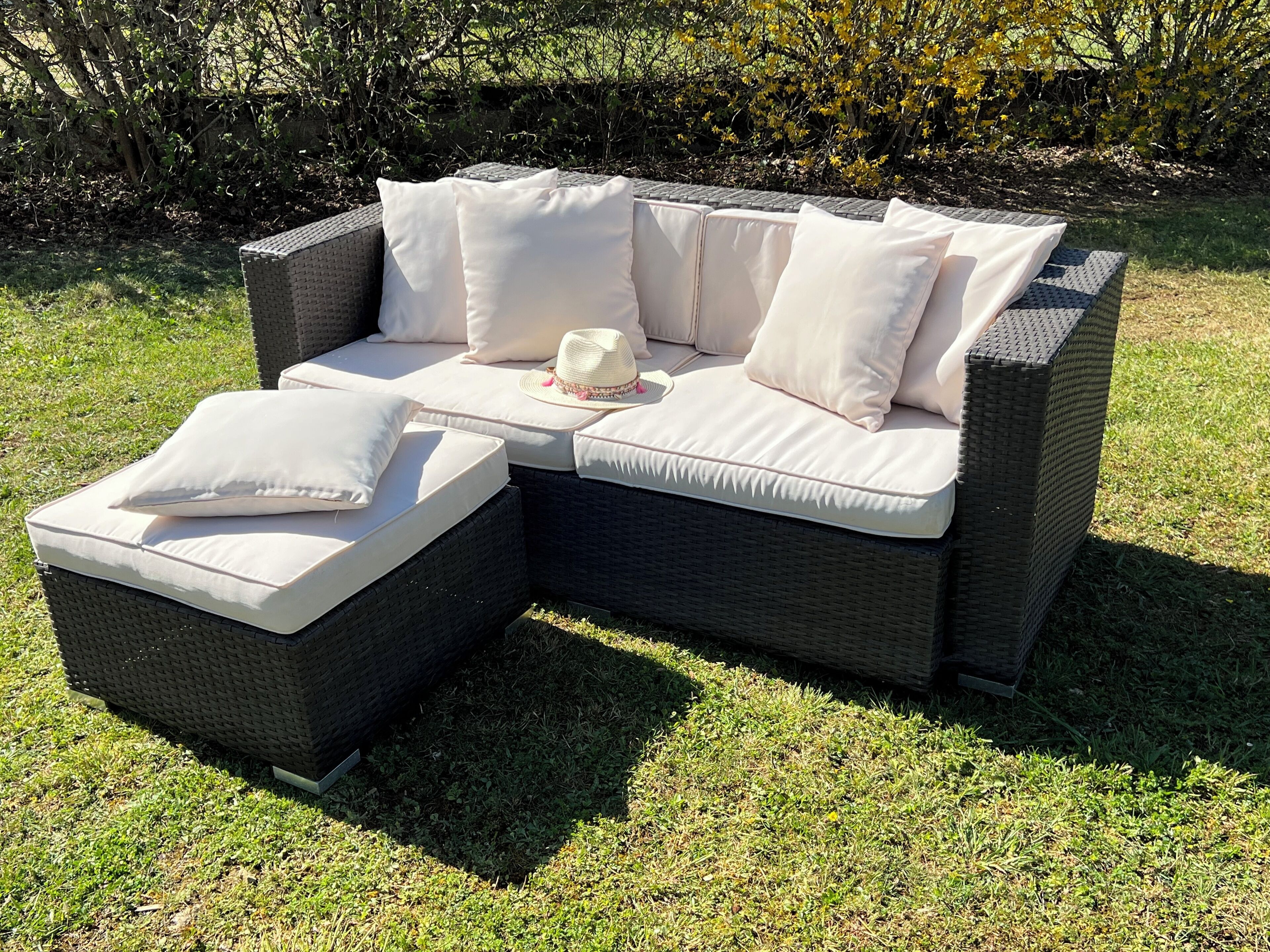 A sectional outdoor sofa with white cushions and a matching ottoman, set on a grassy lawn.