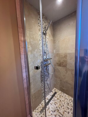 Een douche met glazen wanden, een betegelde vloer en een metalen douchekop.