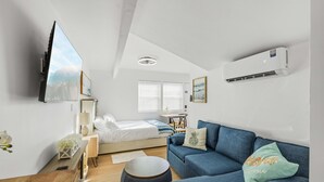 Ein modernes, gut beleuchtetes Zimmer mit einem Bett, einem blauen Sofa, einem Holztisch und einem wandmontierten Fernseher.