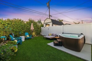 A backyard with artificial grass, a hot tub, outdoor furniture, and a shed.