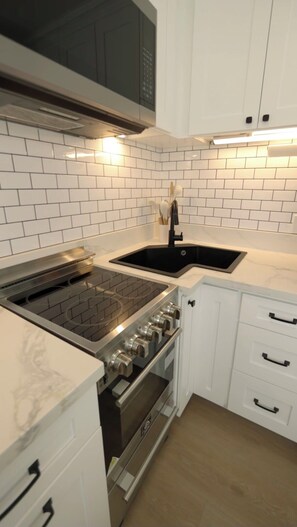 A kitchen with white cabinets, a black sink, a stainless steel stove, and a microwave.