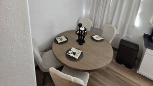 Ein Essbereich mit einem runden Tisch, vier Stühlen, einem schwarzen Kerzenhalter und einem Fenster mit Vorhängen.