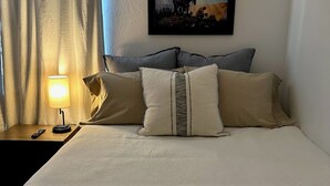 Ein ordentlich bezogenes Bett mit einer beigen Decke, zwei Kissen und einem gerahmten Bild an der Wand.
