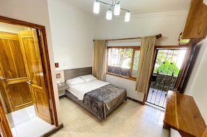 A bedroom with a bed, a window with curtains, a door, and a balcony with a railing.