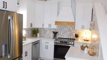 A modern kitchen with white cabinetry, stainless steel appliances, and a small island with seating.
