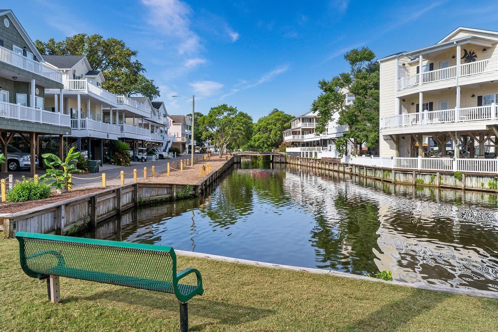 A canal with a bench, buildings on either side, and a clear sky.