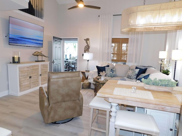 A modern living room with a sofa, a dining table, a chair, a TV, and a ceiling fan. - 1865 All new furnishings sleeps 10 separate loft for children (Myrtle Beach)