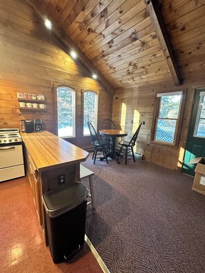A cozy cabin-style kitchen with wooden walls, a central island, and a dining area with chairs. - Enjoy an all seasons retreat, perfect for relaxing getaways in Tamworth NH (Tamworth)