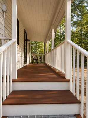 Een houten veranda met witte leuningen, een bank en een deur naar het huis.