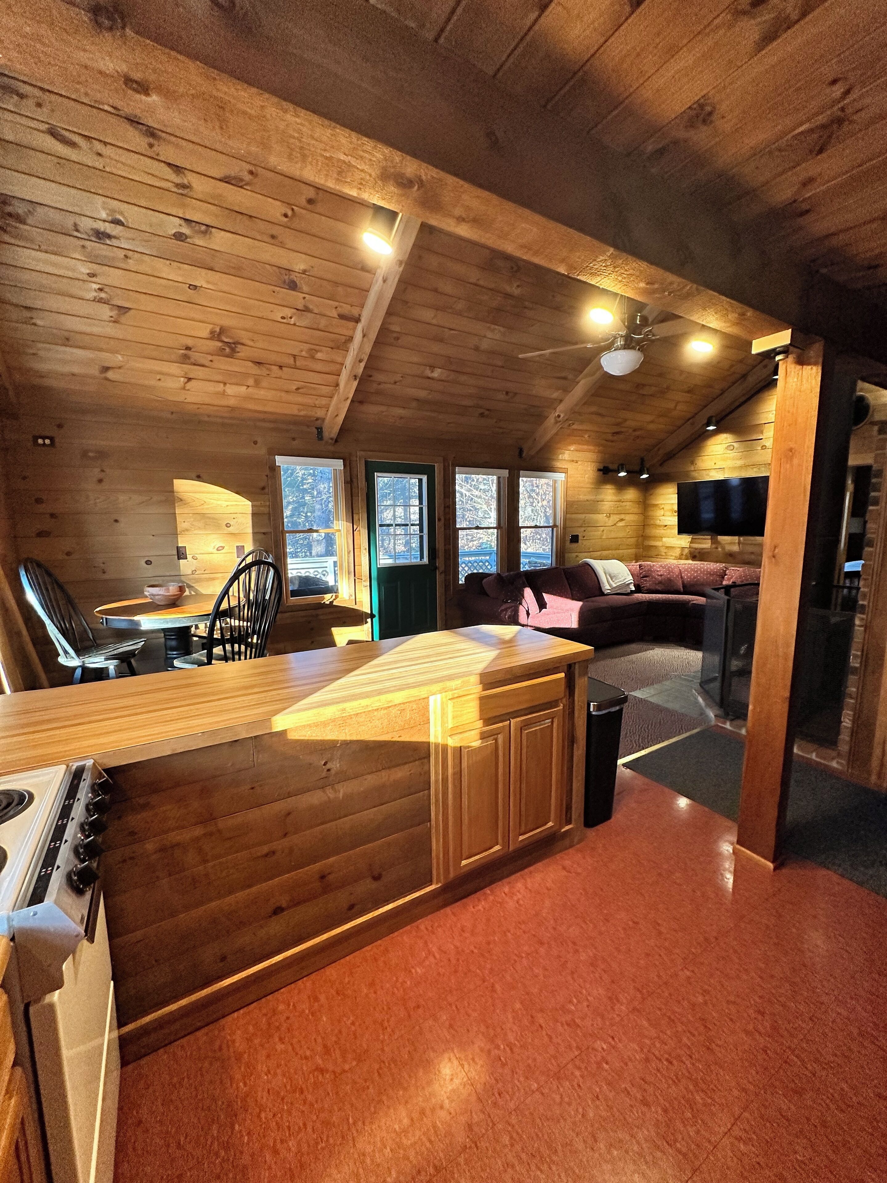 Un intérieur de chalet chaleureux avec une cuisine en bois, un coin repas et un espace de vie comprenant un canapé et un téléviseur.