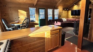 A cozy cabin interior with a wooden kitchen, dining area, and a living space with a sofa and TV. - Enjoy an all seasons retreat, perfect for relaxing getaways in Tamworth NH (Tamworth)