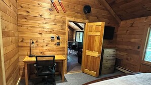 Een gezellig zolderkamer met houten wanden, een bureau met stoel, een bed en een deur naar een andere kamer.