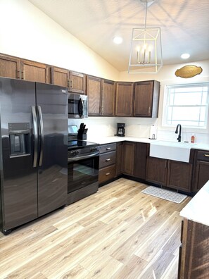 A modern kitchen with stainless steel appliances, wooden cabinets, and a white countertop. - BRAND NEW 3BR Duplex Unit Side “B”, Retreat Near Fort Leonard Wood,Sleeps 8 (Waynesville)