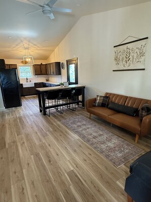 A modern kitchen with dark cabinets, a dining area with a table and chairs, a brown leather sofa, and a ceiling fan. - BRAND NEW 3BR Duplex Unit Side “B”, Retreat Near Fort Leonard Wood,Sleeps 8 (Waynesville)