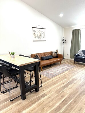 A modern living room with a wooden dining table, black chairs, a brown leather sofa, and a black armchair. - BRAND NEW 3BR Duplex Unit Side “B”, Retreat Near Fort Leonard Wood,Sleeps 8 (Waynesville)