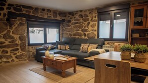 A living room with a stone wall, a sofa, a coffee table, and a dining area with chairs and a table. - Complete 4 Bedroom House near Termas de Bande and Lobios - Villa Limia (Chaos)