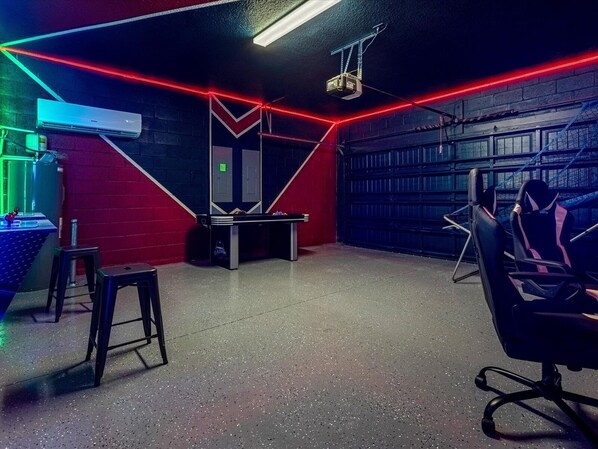 Una sala de juegos con mesa de billar, sillas y un proyector.