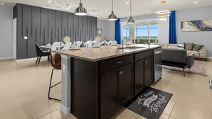 Une cuisine moderne dotée d’un îlot central, de luminaires suspendus et d’un coin repas avec chaises et tables.