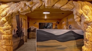 Un hall d’entrée avec un comptoir de réception, des murs en pierre et des œuvres d’art représentant un paysage désertique et une figure vêtue d’un costume traditionnel.