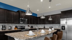 Une cuisine moderne avec des meubles de couleur sombre, un réfrigérateur en acier inoxydable, un comptoir en granit et un coin bar avec des tabourets.