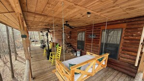 A wooden cabin with a porch, a swing chair, and a table.