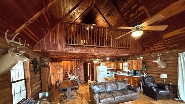 A rustic cabin interior with a dining area, a sofa, a fireplace, and a kitchen.