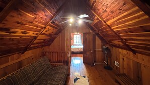 A cozy attic bedroom with a wooden ceiling, a bed, a bench, and a ceiling fan.