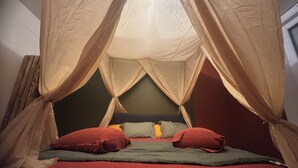 Una cama con una manta y almohadas rojas, una pared verde y una ventana con cortinas.