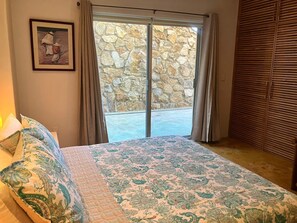 A bedroom with a bed, a framed picture on the wall, a stone wall, and a wooden closet.