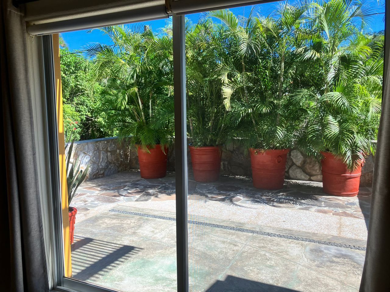 Une vue à travers une fenêtre donnant sur un mur de pierre et des plantes en pot.