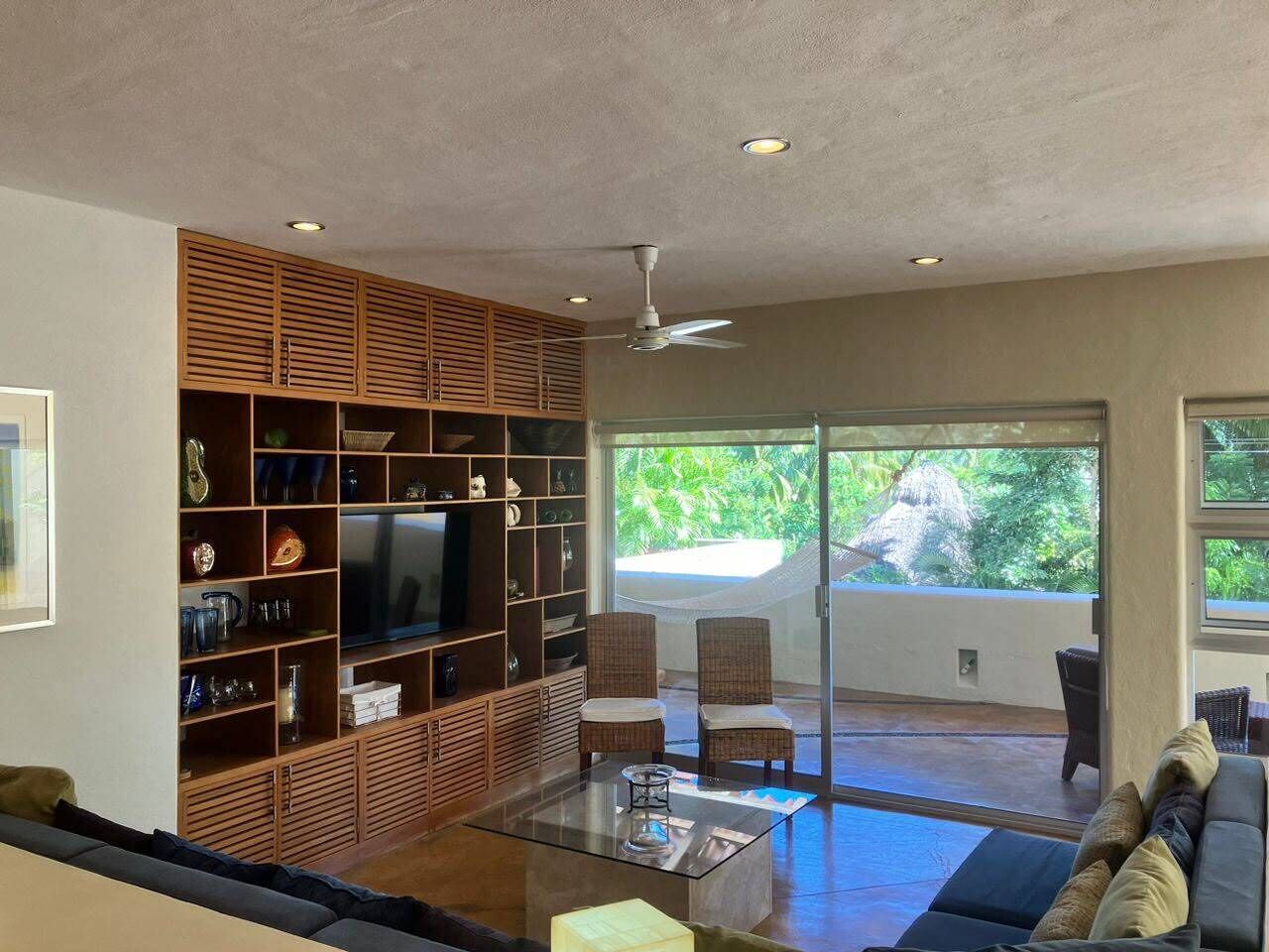 A living room with a TV, shelves, wicker chairs, and a glass coffee table.
