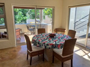 A dining area with a round table, wicker chairs, and a view through glass doors.