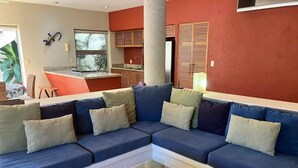 Ein Wohnzimmer mit einer Eckcouch, einem Couchtisch und einer dahinterliegenden Küchenzeile.