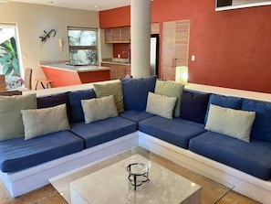 A living room with a sectional sofa, a coffee table, and a kitchen area in the background.