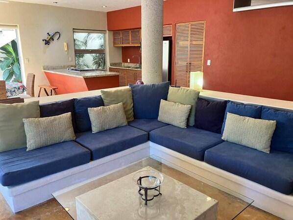 A living room with a sectional sofa, a coffee table, and a kitchen area in the background.