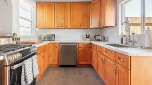 A modern kitchen with wooden cabinets, a gas stove, a dishwasher, and a large window providing natural light. - Overlook Heights Retreat in beautiful San Diego by USD (San Diego)
