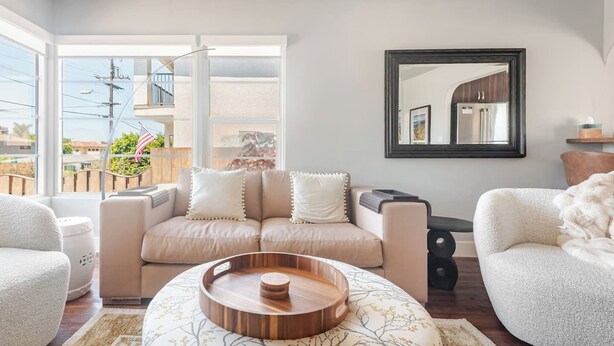 A modern living room with a beige sofa, a round wooden coffee table, and a large mirror on the wall. - Overlook Heights Retreat in beautiful San Diego by USD (San Diego)