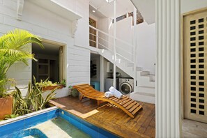 A wooden lounge chair by a pool with a staircase leading to an upper level. - Casa Mary - Beautiful 5BR House in the Old City (Cartagena de Indias)