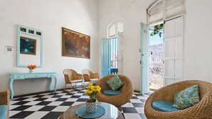 Una stanza con pavimento a scacchi, mobili in vimini, un tavolino consolle blu e un quadro appeso al muro.