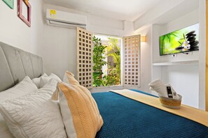 A hotel room with a bed, a TV mounted on the wall, and a window with a view of greenery. - Casa Mary - Beautiful 5BR House in the Old City (Cartagena de Indias)