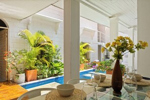 A dining area with a pool view, white columns, and potted plants. - Casa Mary - Beautiful 5BR House in the Old City (Cartagena de Indias)