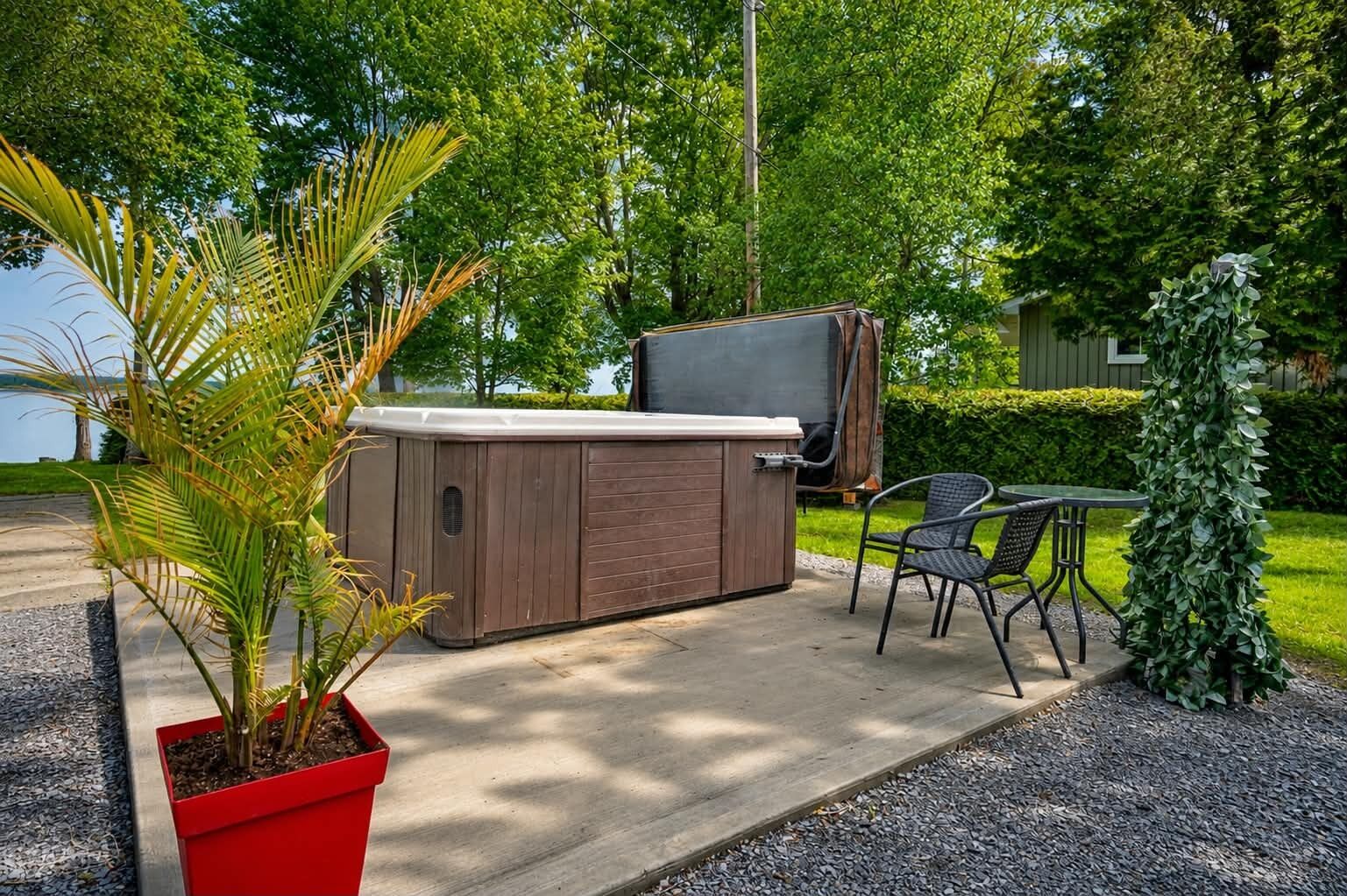Un bain à remous avec un revêtement extérieur en bois, un barbecue couvert et un espace détente avec des chaises.